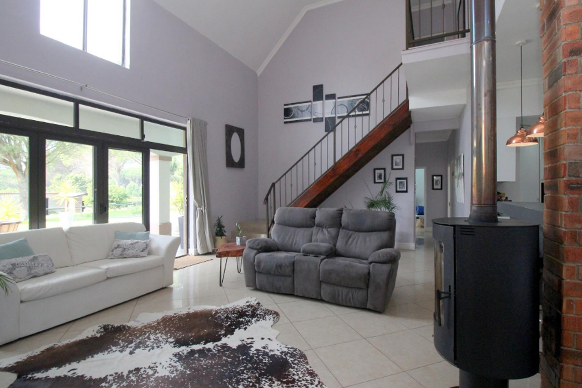 Spacious living room featuring a vaulted ceiling, tiled floors, a striking exposed brick pillar, and a modern freestanding wood-burning fireplace with staircase access.