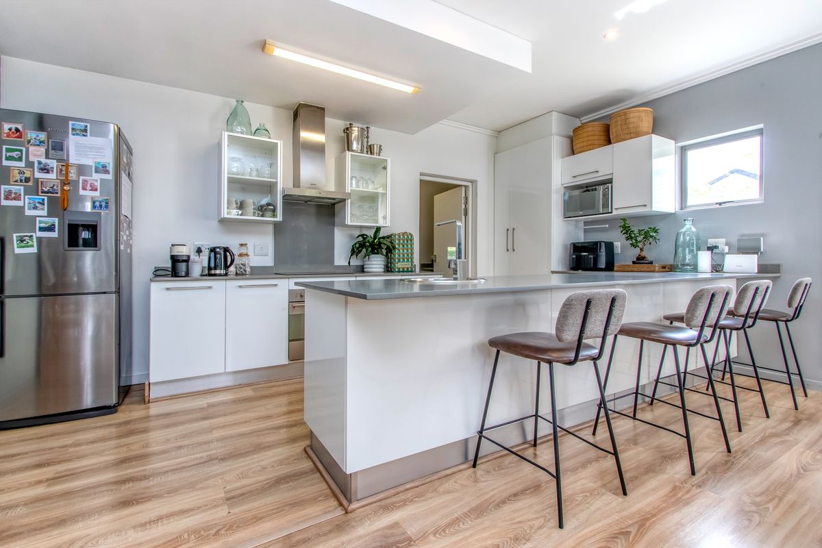 Modern kitchen featuring white cabinetry, a central island with breakfast bar seating, stainless steel extractor fan, and integrated microwave.