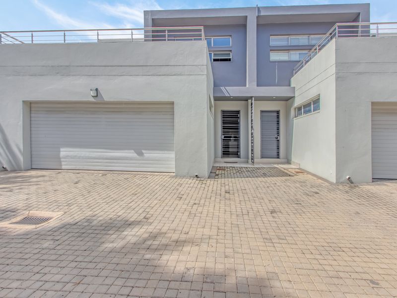 Modern double-story residential facade featuring a paved driveway, double garage, and upper-level balcony with stainless steel railings.