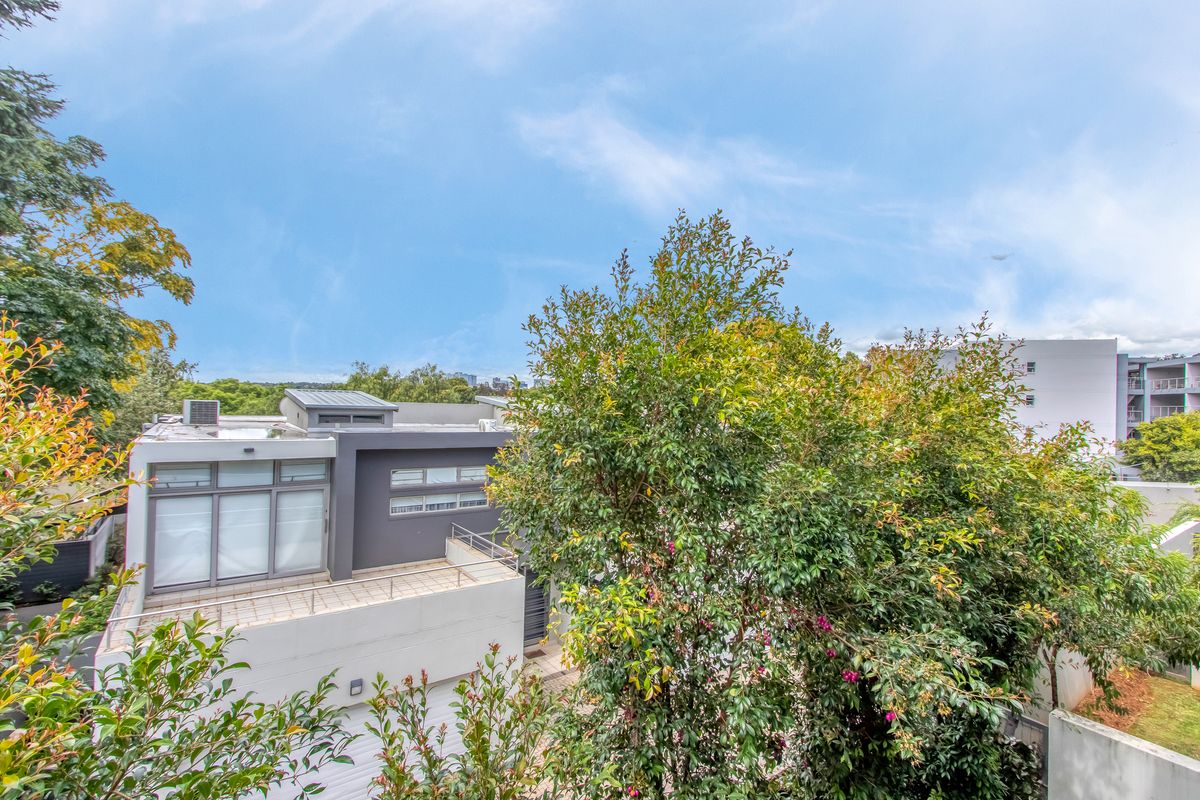 An elevated view of a modern residential property featuring a flat roof design, balcony, and contemporary exterior finishes surrounded by mature trees.
