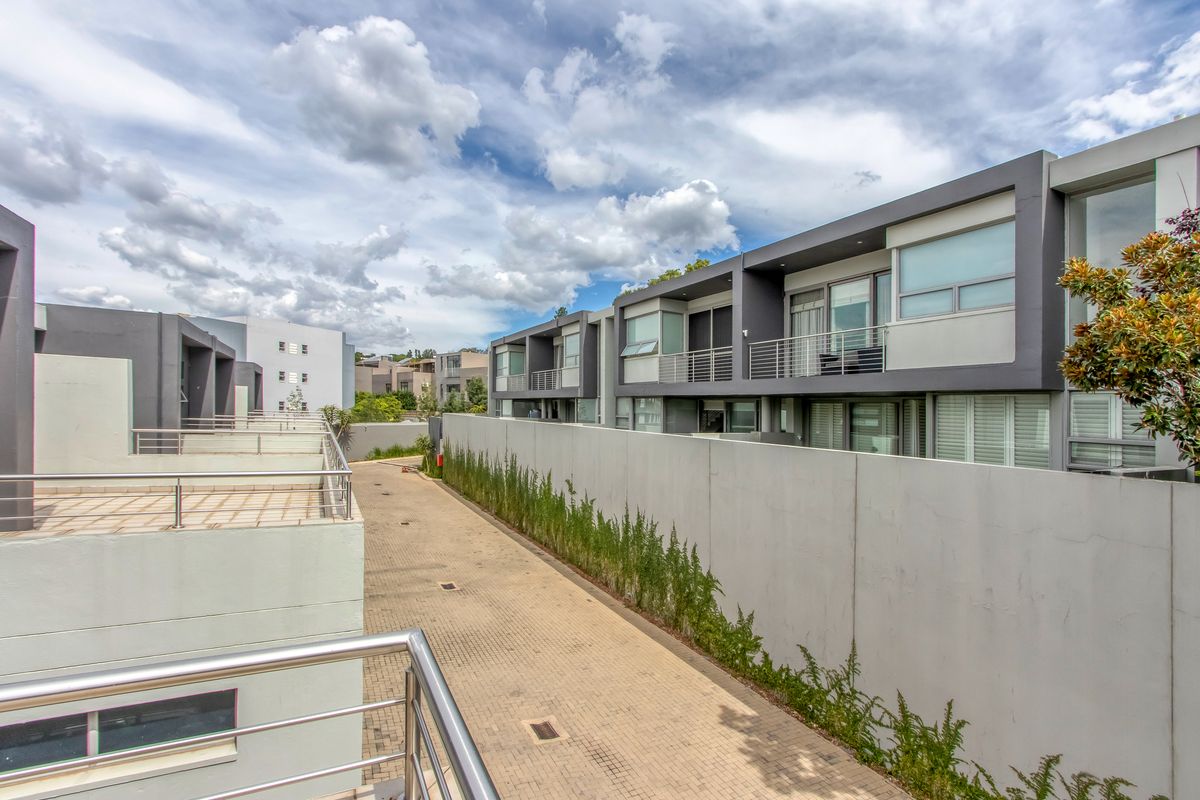 View of a modern residential complex featuring paved driveway, contemporary multi-story townhouses with balconies, and clean architectural lines.