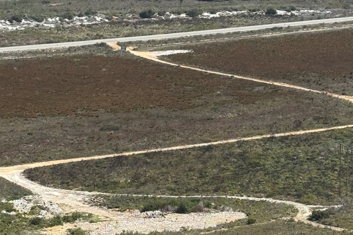 An aerial view of the expansive farm landscape featuring dirt access roads, natural vegetation, and distant coastal scenery.