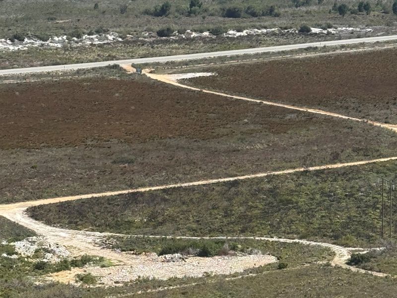 An aerial view of the expansive farm landscape featuring dirt access roads, natural vegetation, and distant coastal scenery.