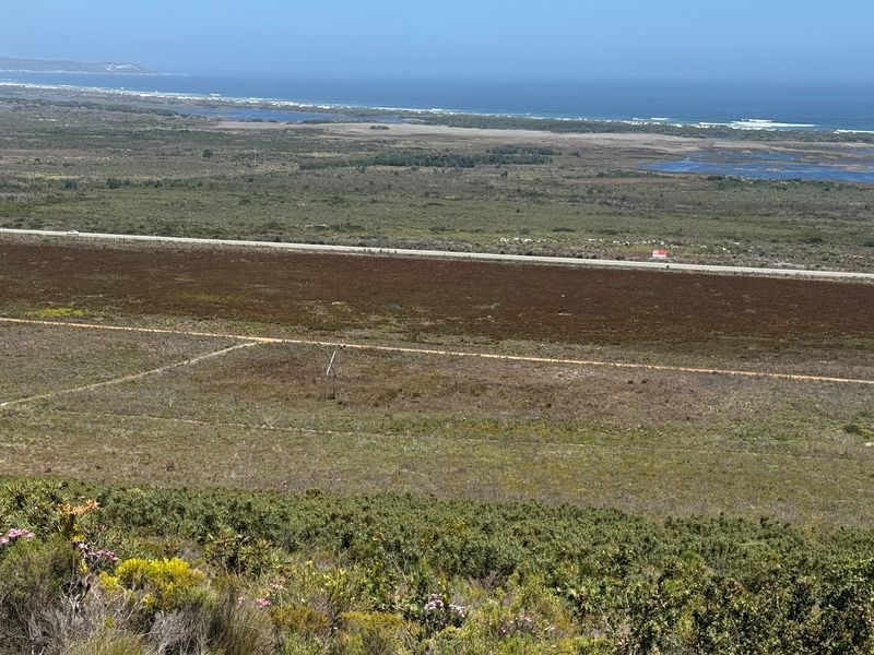 Expansive elevated view overlooking natural coastal landscape, open fields, and the distant ocean horizon.