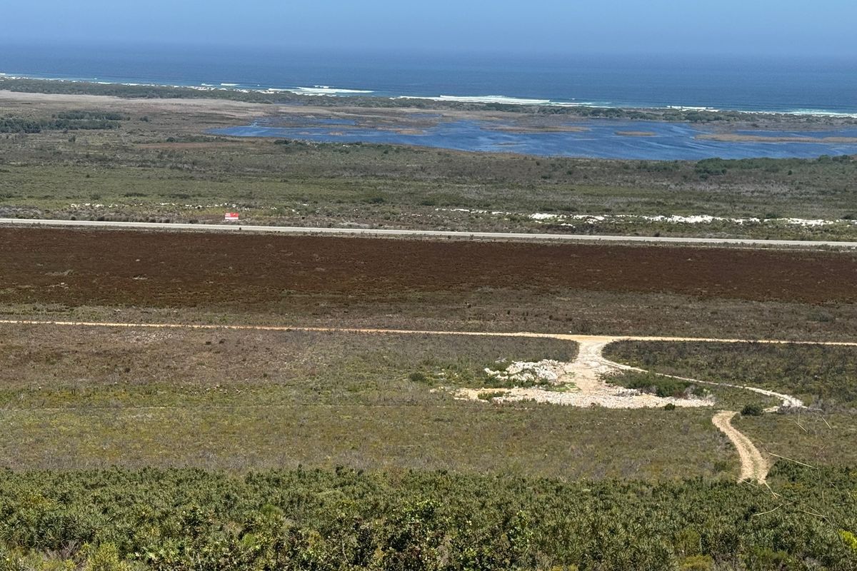 An elevated panoramic view of the surrounding farm landscape, featuring natural vegetation, a dirt access road, and distant coastal scenery.