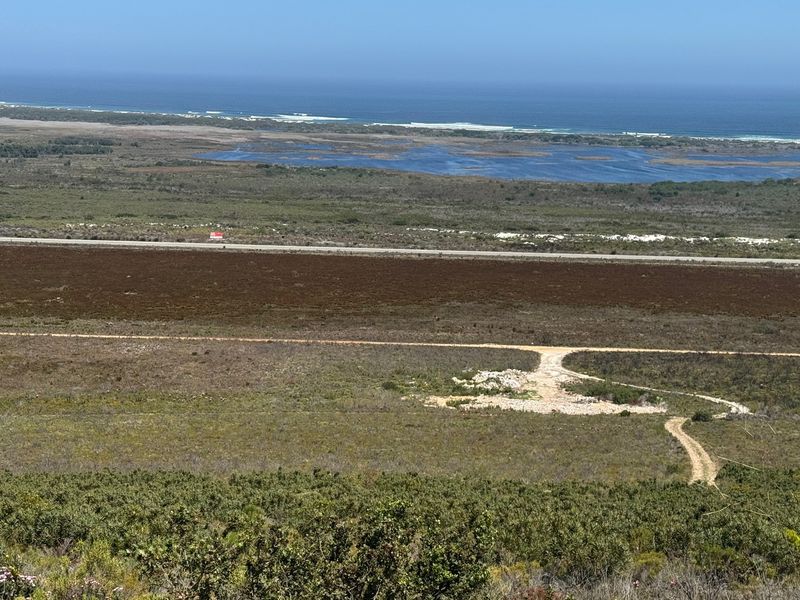 An elevated panoramic view of the surrounding farm landscape, featuring natural vegetation, a dirt access road, and distant coastal scenery.