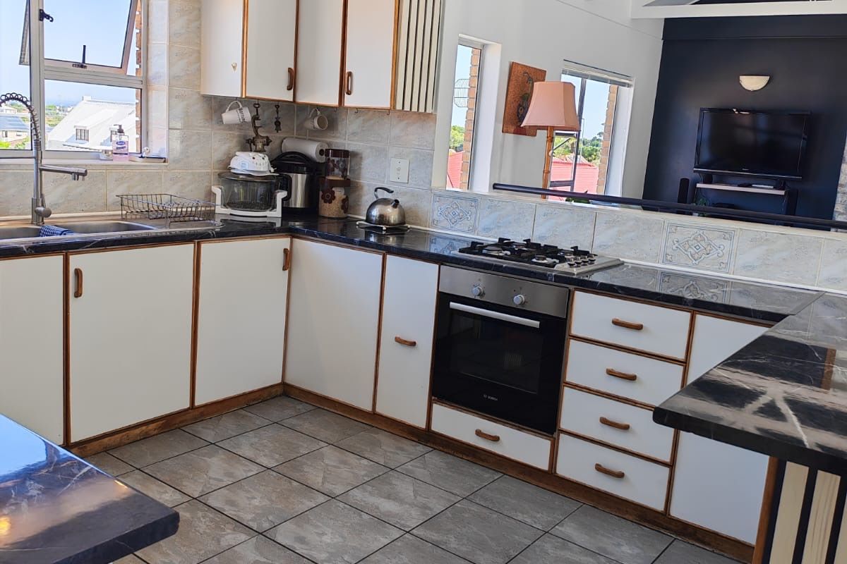 A functional kitchen featuring white cabinetry with wood trim, dark stone-look countertops, a built-in oven, gas hob, and tiled flooring under a vaulted ceiling.