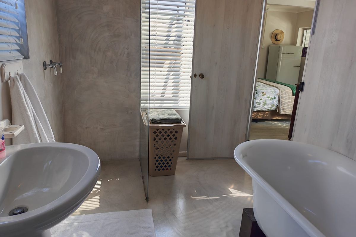 A bathroom featuring a pedestal sink and a freestanding bathtub, with concrete-style wall finishes and a view into the adjacent bedroom.