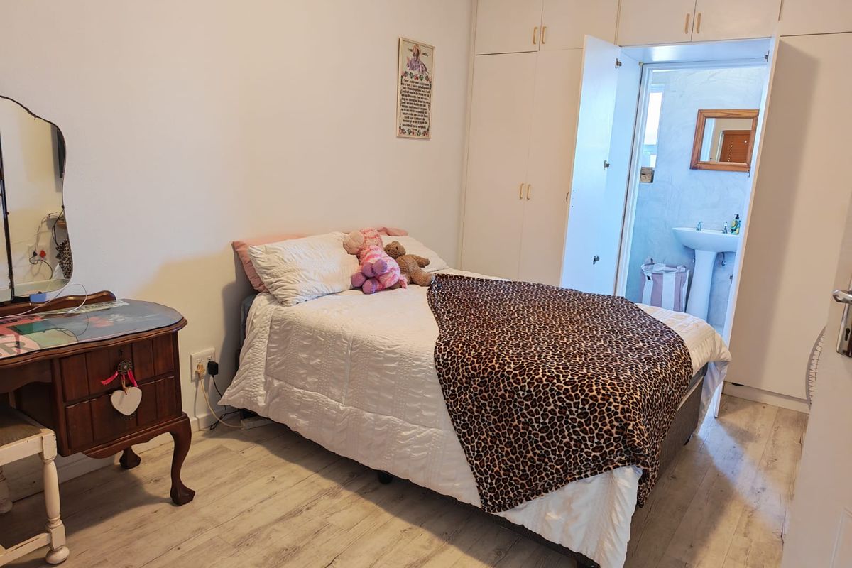 A bedroom featuring built-in cupboards and an en-suite bathroom with a pedestal basin, finished with light-toned laminate flooring.
