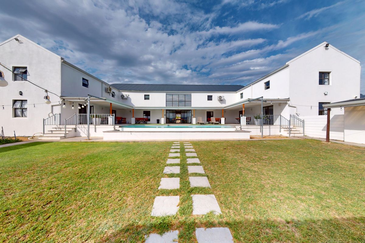 Spacious U-shaped farm property featuring a central swimming pool, paved patio areas, and a well-maintained lawn in a serene outdoor setting.
