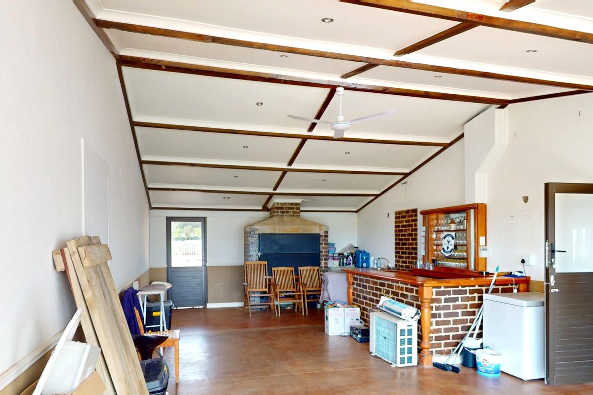 Spacious entertainment area featuring a built-in brick bar, exposed timber ceiling beams, and a traditional brick fireplace, offering a versatile rustic living space.