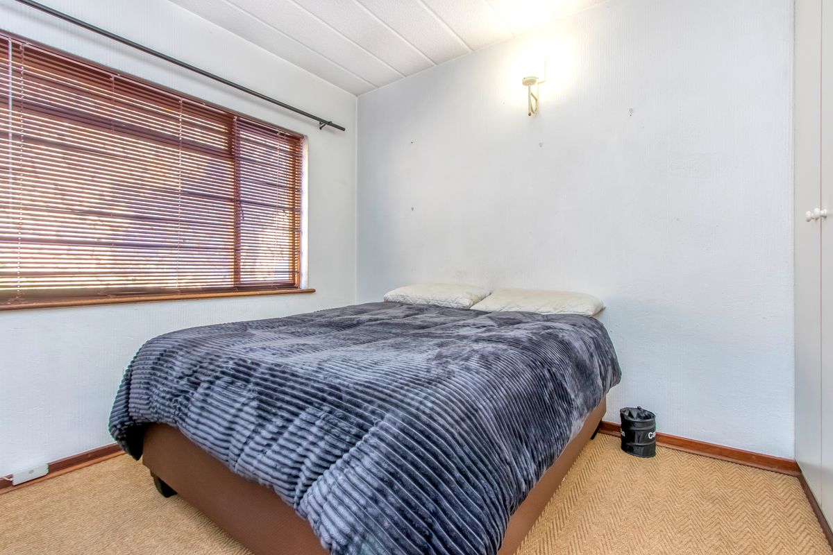 A bedroom featuring a large window with fitted venetian blinds, textured ceiling, and built-in wardrobe storage.