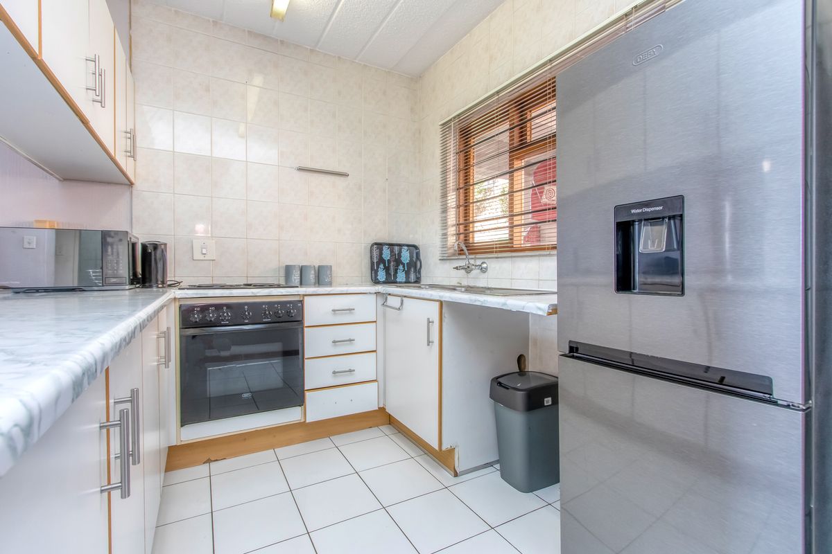 A functional kitchen featuring white cabinetry, tiled walls, a built-in oven with hob, and a stainless steel sink.