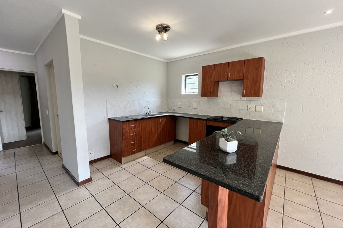 A functional kitchen featuring dark granite countertops, wood-finish cabinetry, a built-in hob, and tiled flooring in an open-plan layout.