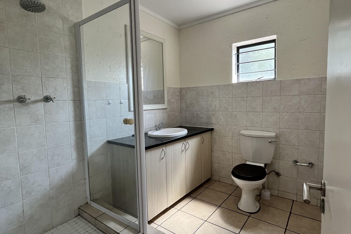 A functional bathroom featuring a glass-enclosed shower, a vanity with a basin, and a toilet, finished with neutral wall and floor tiling.