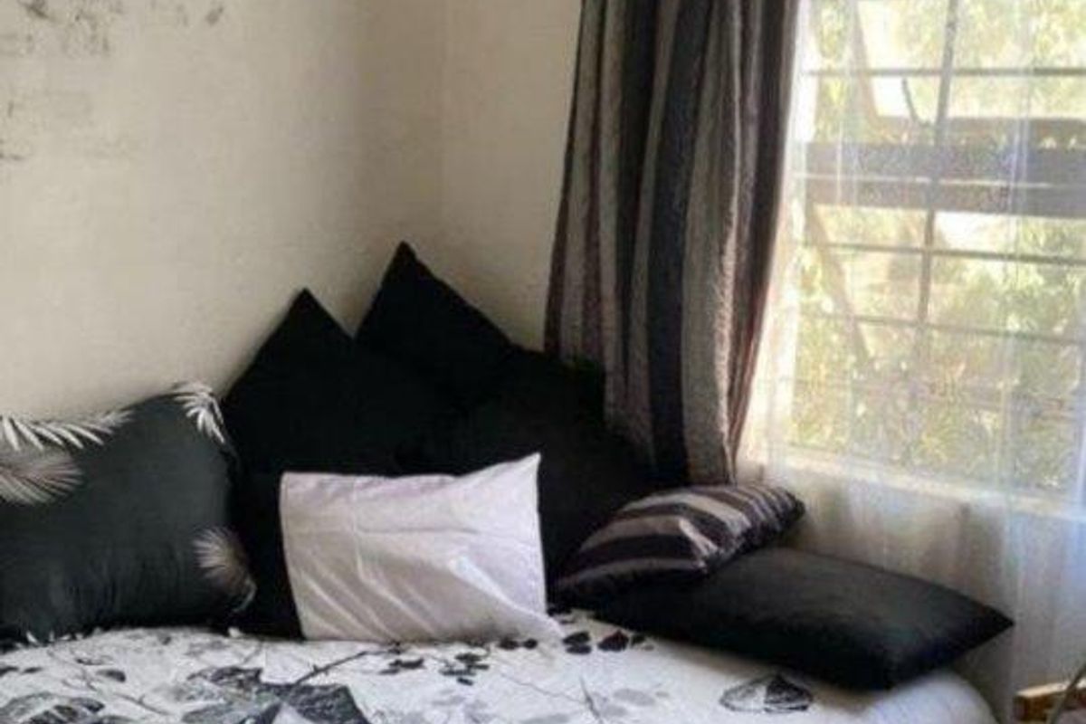 A bedroom featuring a window with security bars and curtains, requiring cosmetic updates to the wall finishes.
