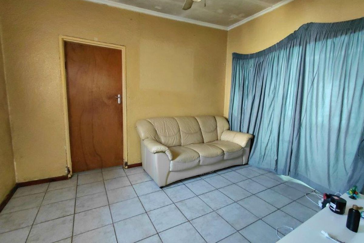A living room featuring tiled flooring, a ceiling fan, and a wooden door, requiring cosmetic updates to improve its overall appeal.
