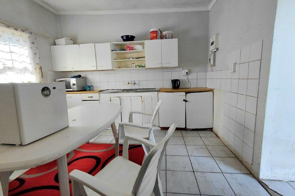 A functional kitchen featuring white cabinetry, tiled splashbacks, and tiled flooring, offering a basic layout ready for potential modernization.
