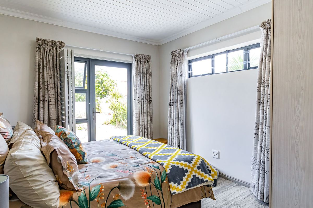 A bright bedroom featuring a built-in wardrobe, tongue and groove ceiling, and direct access to the garden through a glass door.