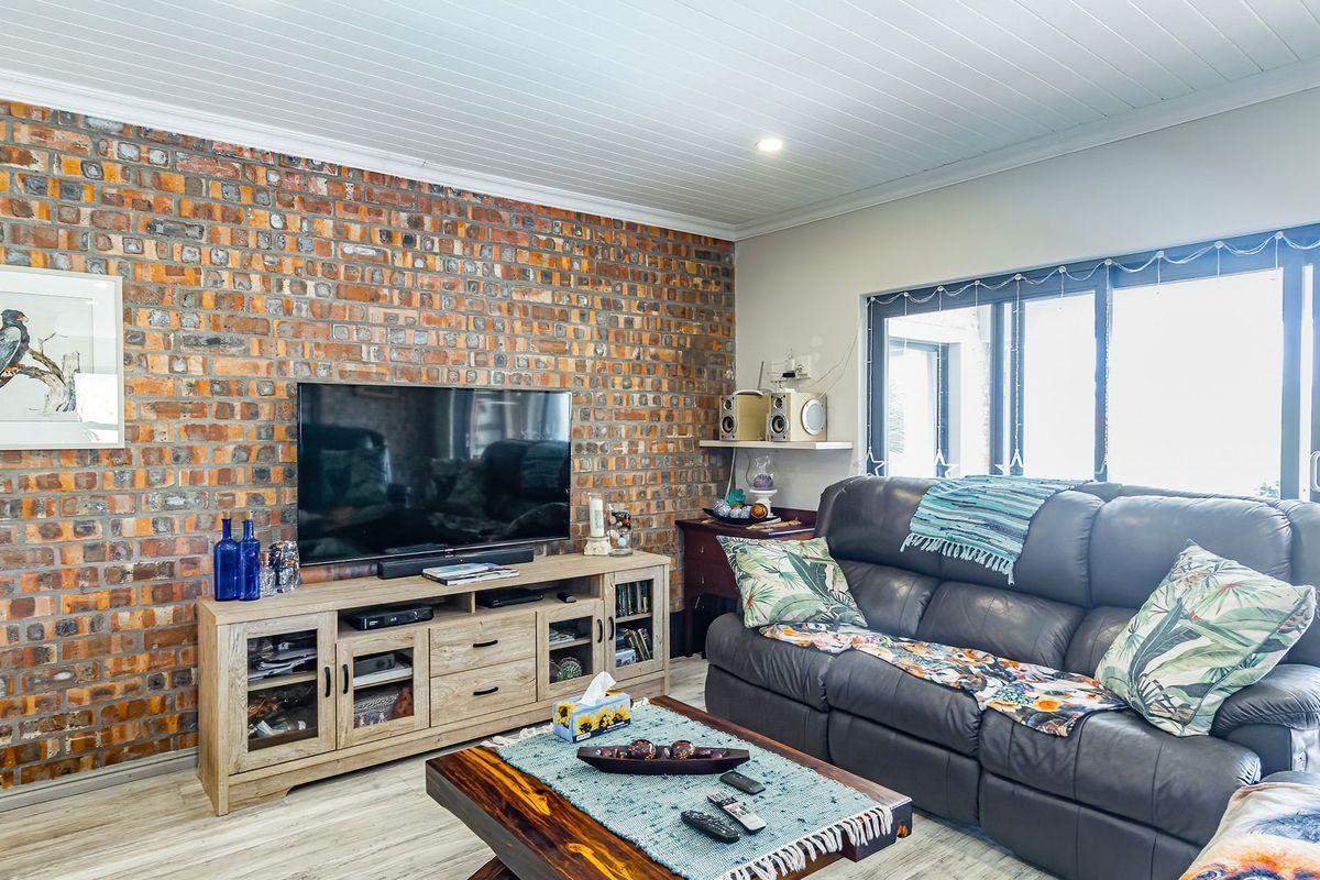 A comfortable living room featuring an exposed brick feature wall, light timber-look flooring, and a tongue and groove ceiling with access to outdoor space.