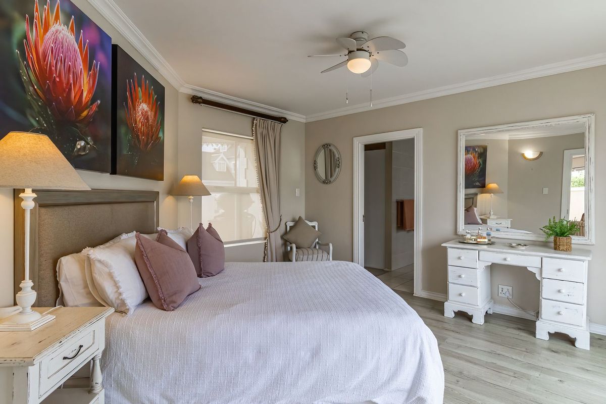 A well-maintained bedroom featuring light wood-look flooring, crown molding, a ceiling fan, and an en-suite bathroom entrance.