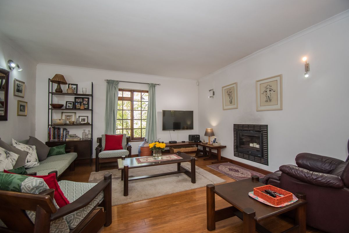 A comfortable living room featuring polished timber flooring, a built-in fireplace, and large windows that provide natural light.