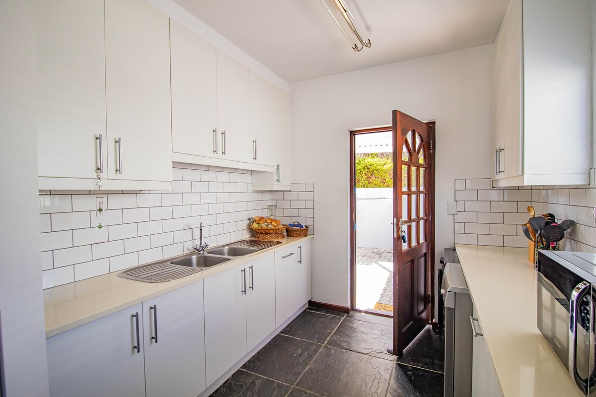 A functional kitchen featuring white cabinetry, subway tile backsplash, stone countertops, and a double stainless steel sink, with direct access to the exterior.