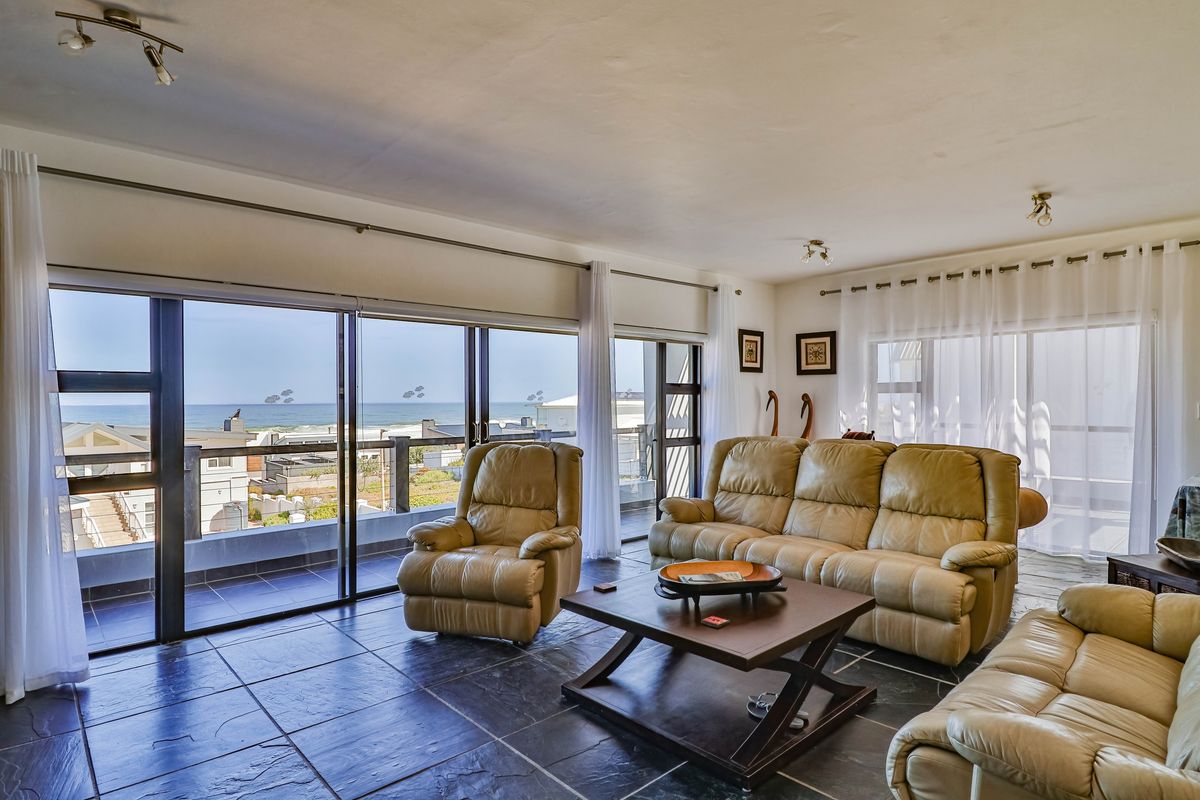 Spacious living area featuring large sliding glass doors that open to a balcony with expansive ocean views and dark tiled flooring.