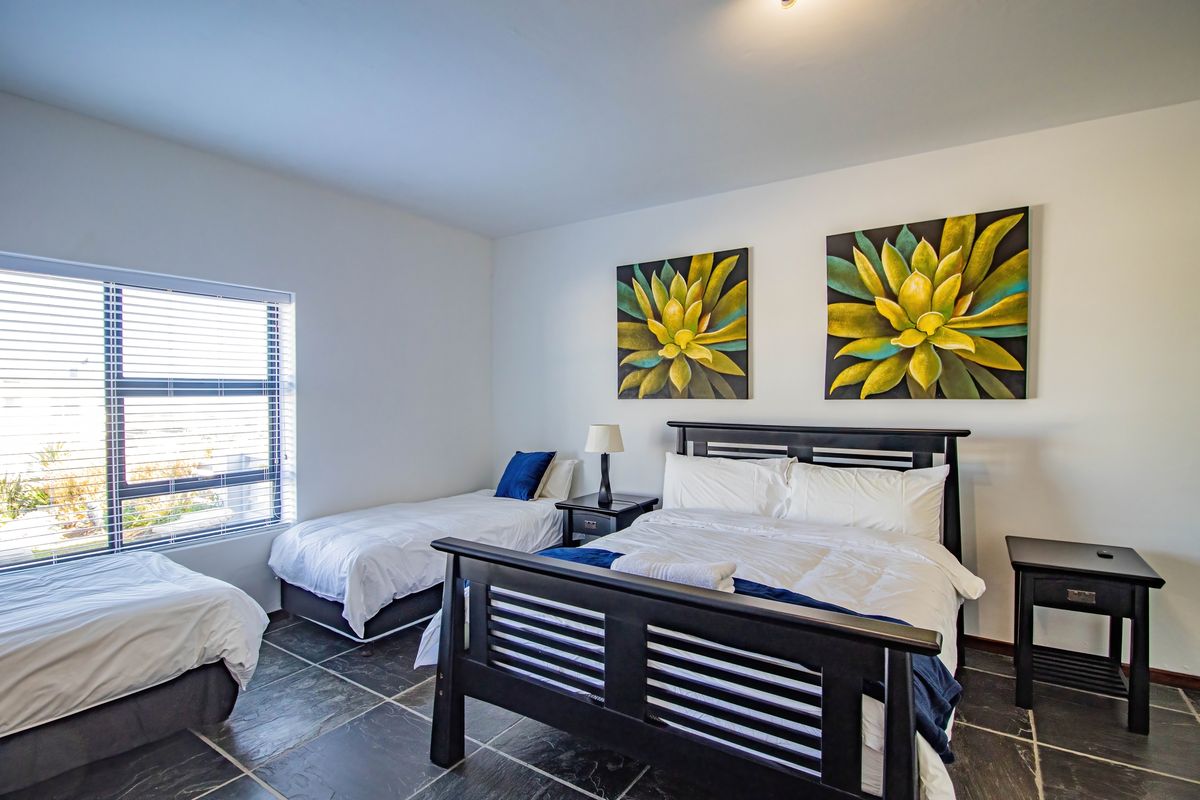 A spacious bedroom featuring tiled flooring, large windows with fitted blinds, and neutral wall finishes.