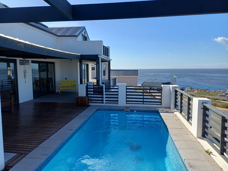 An elevated outdoor pool area featuring timber decking, a modern metal balustrade, and a covered patio with expansive ocean views.