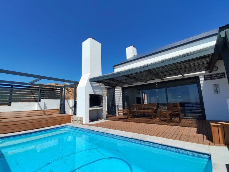 Outdoor entertainment area featuring a swimming pool, timber decking, and a built-in braai under a pergola, adjacent to the main living space.