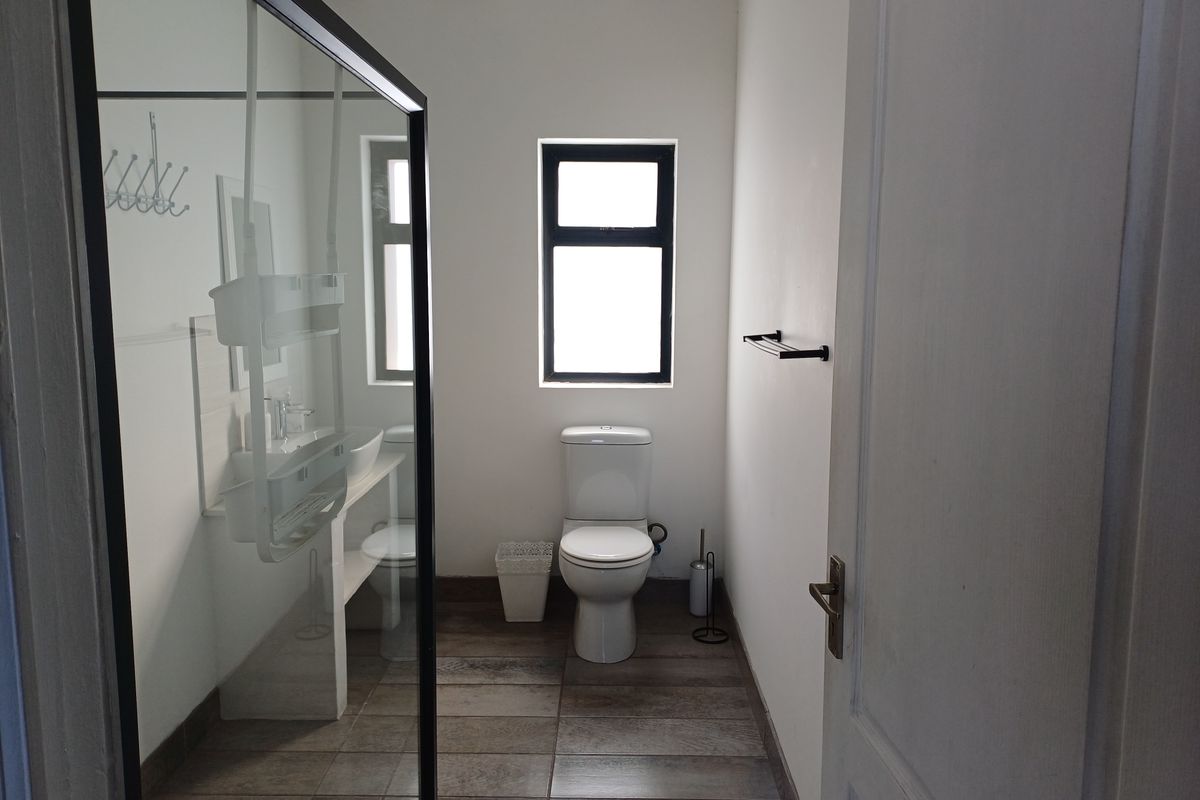 A modern bathroom featuring a glass-enclosed shower, a white toilet, a vanity basin, and dark wood-look floor tiles.