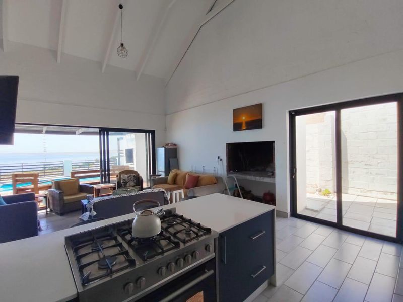 Spacious open-plan living area featuring a vaulted ceiling, modern kitchen island with gas stove, built-in fireplace, and seamless access to the outdoor patio.