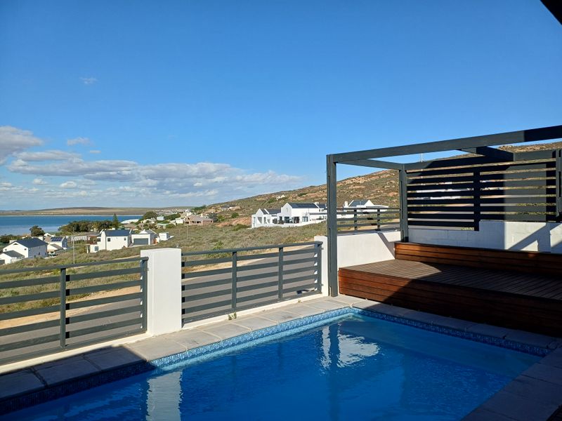 A modern outdoor pool area featuring a built-in timber deck, pergola, and metal balustrade, offering scenic coastal and landscape views.