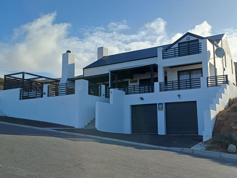 A modern two-story house featuring a double garage, balcony, and clean white exterior finishes, situated on a sloped street-facing lot.