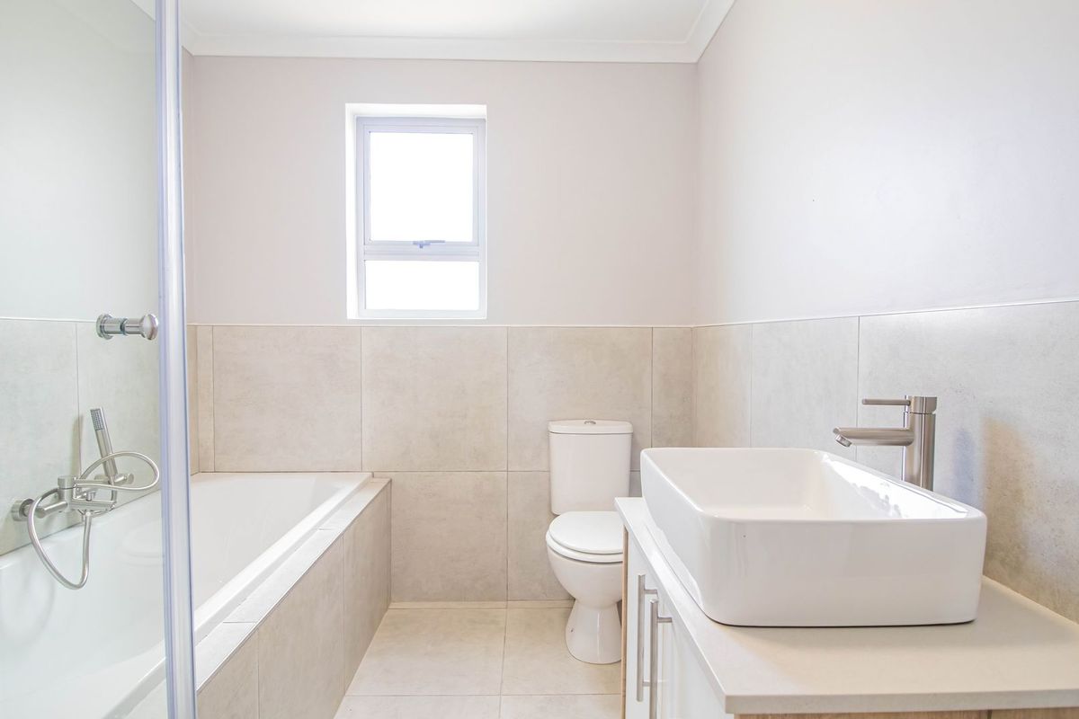 A modern, neutral-toned bathroom featuring a built-in bathtub with shower mixer, a contemporary vessel sink on a vanity, and a standard toilet.