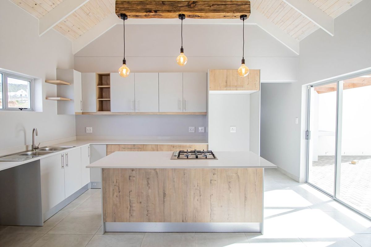 Modern open-plan kitchen featuring a central island with a built-in gas hob, light wood cabinetry, stone countertops, and vaulted ceilings with pendant lighting.