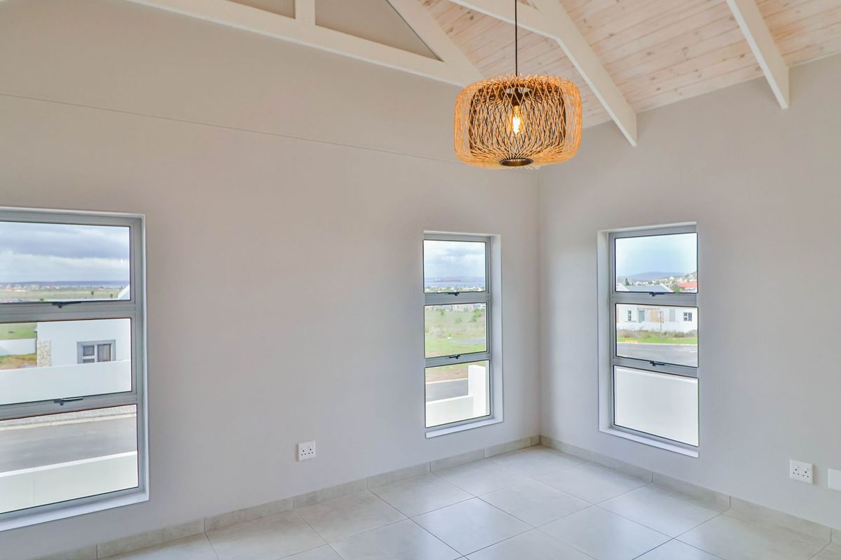 A bright, empty bedroom featuring high vaulted ceilings with exposed beams, tiled flooring, and multiple windows offering natural light and neighborhood views.
