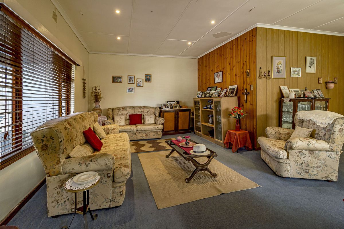A spacious living room featuring wood-paneled accent walls, recessed ceiling lighting, and large windows with fitted blinds.