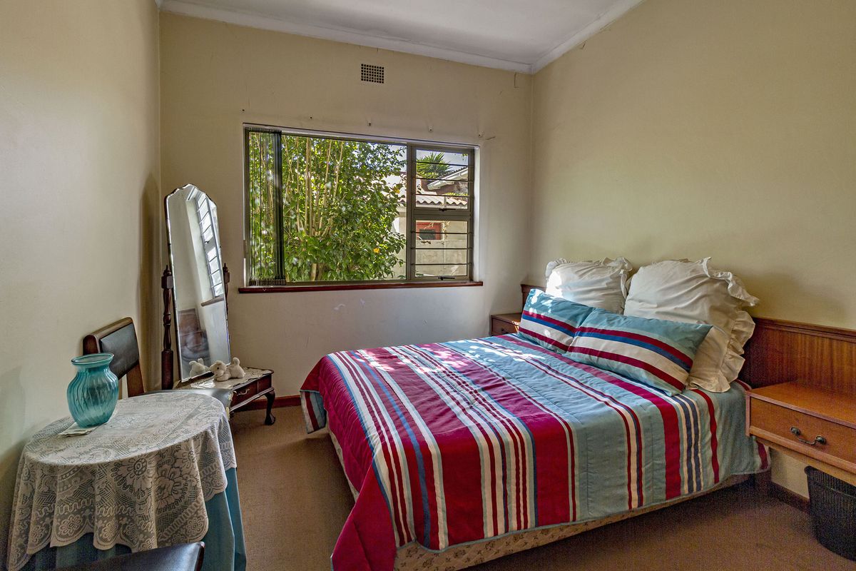 A functional bedroom featuring a built-in wooden headboard and side tables, carpeted flooring, and a large window providing natural light.