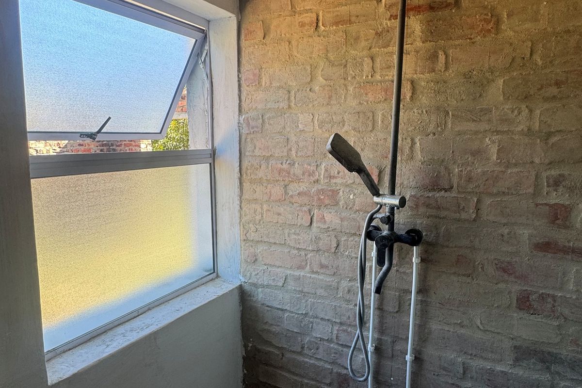 A rustic-style shower area featuring an exposed brick wall, modern black rainfall showerhead, and frosted glass window.