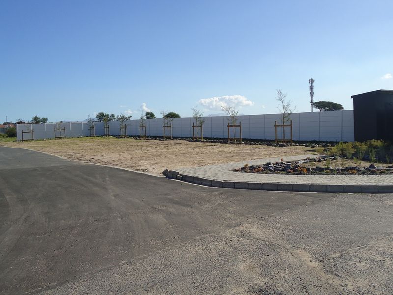 A view of the entrance area of a townhouse development, featuring a paved driveway, boundary wall, and security gatehouse structure.