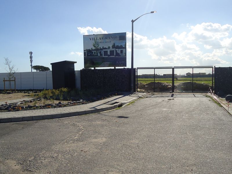 Front entrance view of the property featuring a secure metal gate, perimeter walling, and paved driveway access.