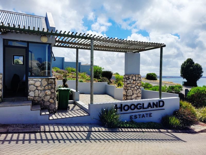 Entrance facade of Hoogland Estate featuring stone cladding, a timber pergola, and paved driveway with coastal views.