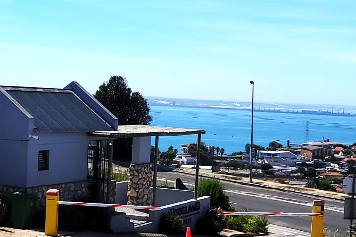 Entrance to the residential estate featuring a security boom gate, guard house, and paved driveway with scenic coastal views.