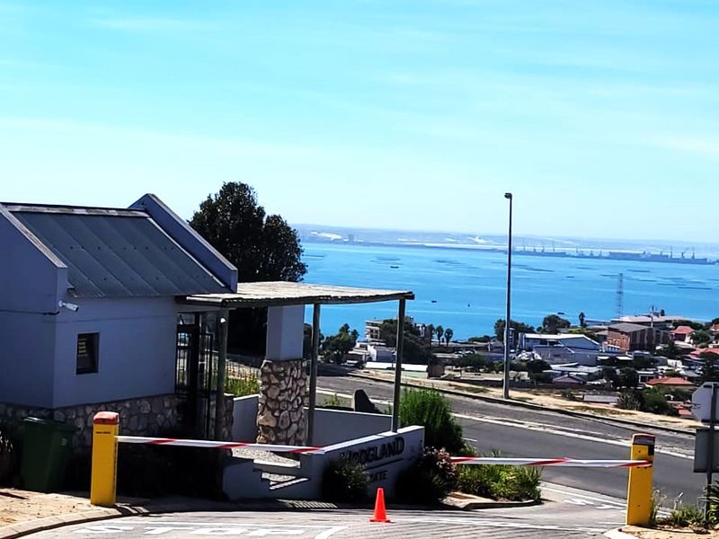 Entrance to the residential estate featuring a security boom gate, guard house, and paved driveway with scenic coastal views.