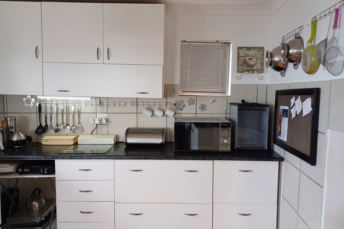 A functional kitchen area featuring white cabinetry, dark laminate countertops, and a tiled backsplash with integrated storage solutions.