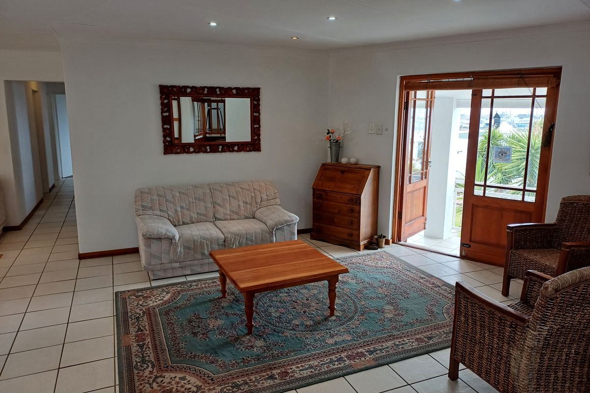 A bright living room featuring ceramic floor tiles, recessed ceiling lighting, and wooden framed glass doors leading to an outdoor area.