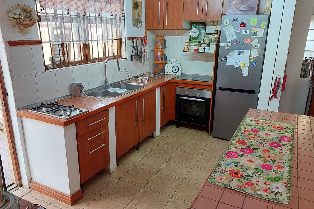 A functional kitchen featuring wood-finish cabinetry, tiled countertops, a built-in oven, and a stainless steel sink, offering a practical layout for daily meal preparation.