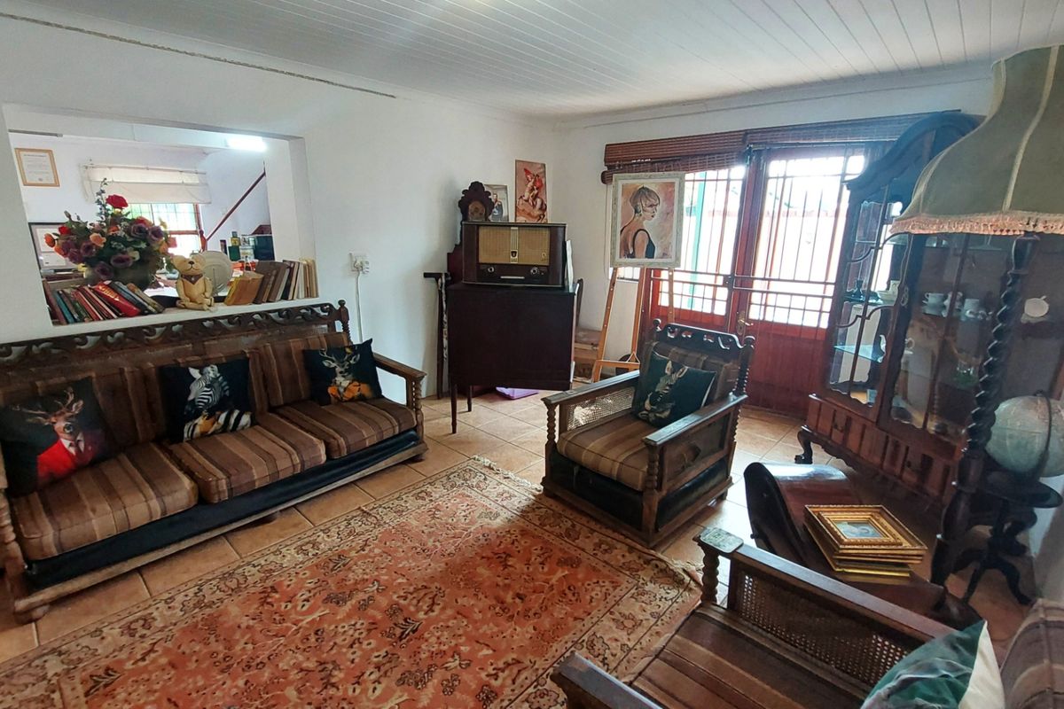A living room featuring tiled flooring, a timber-framed glass door, and a large opening connecting to an adjacent room.